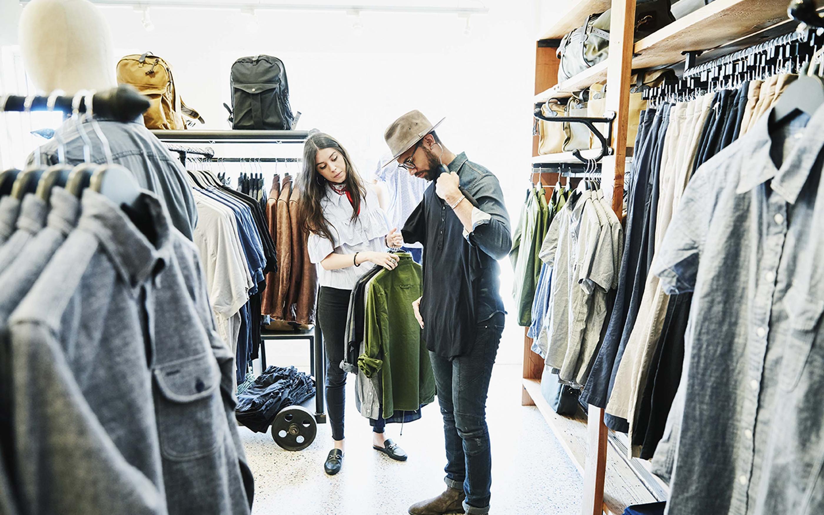Shopkeeper helping man decide on shirts while shopping in mens clothing boutique