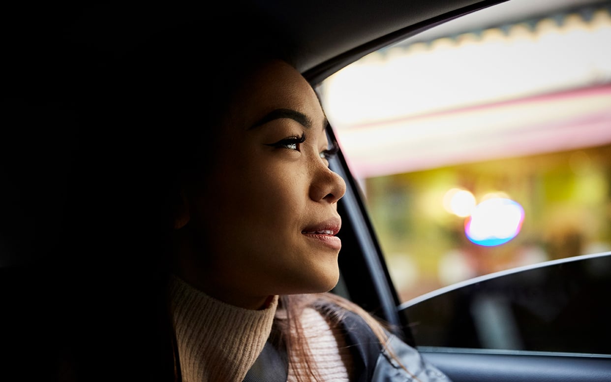 A person looking out of a car window at a city skyline reflecting in the glass.