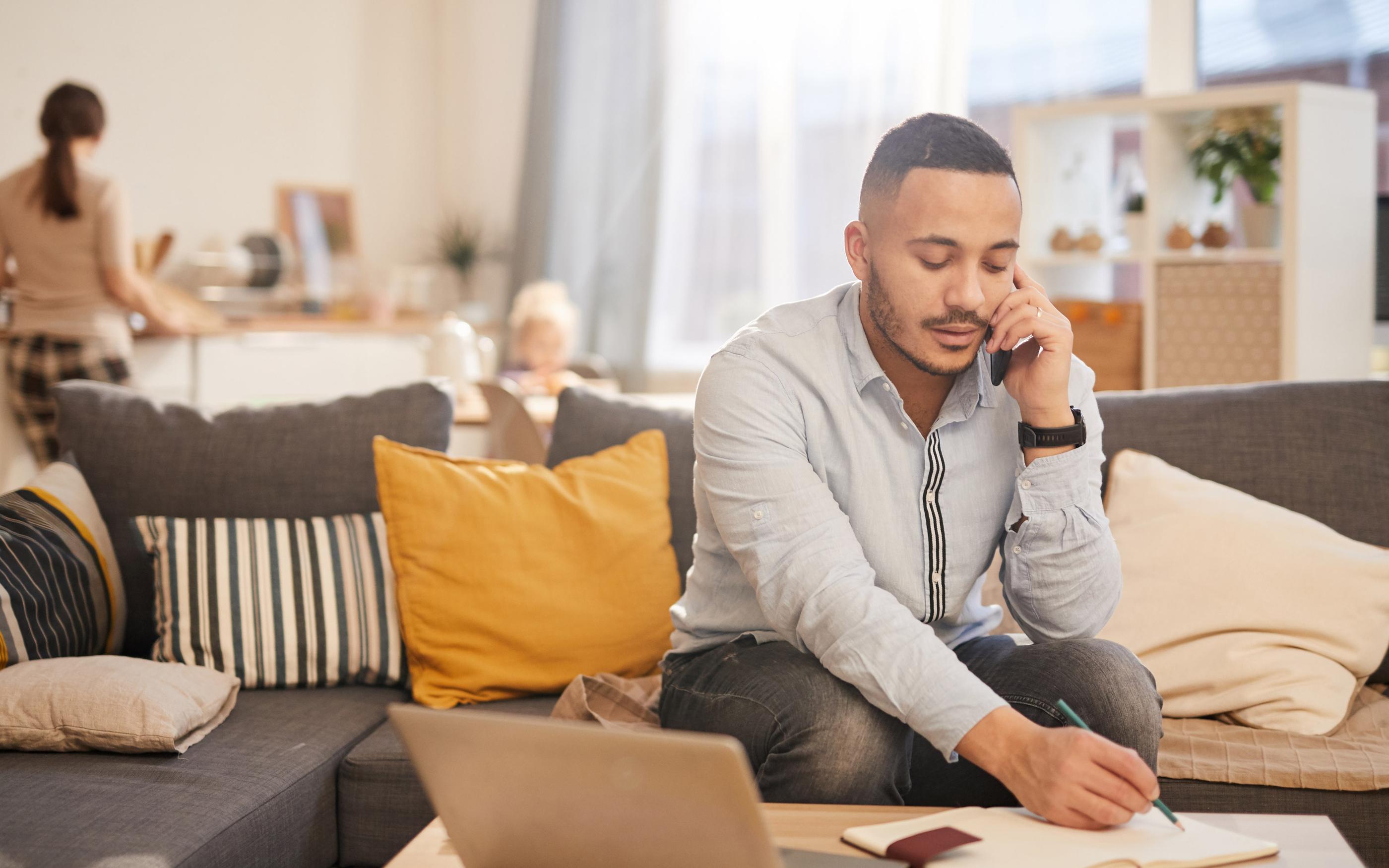 Portrait of modern mixed race man speaking by phone while working from home in cozy interior