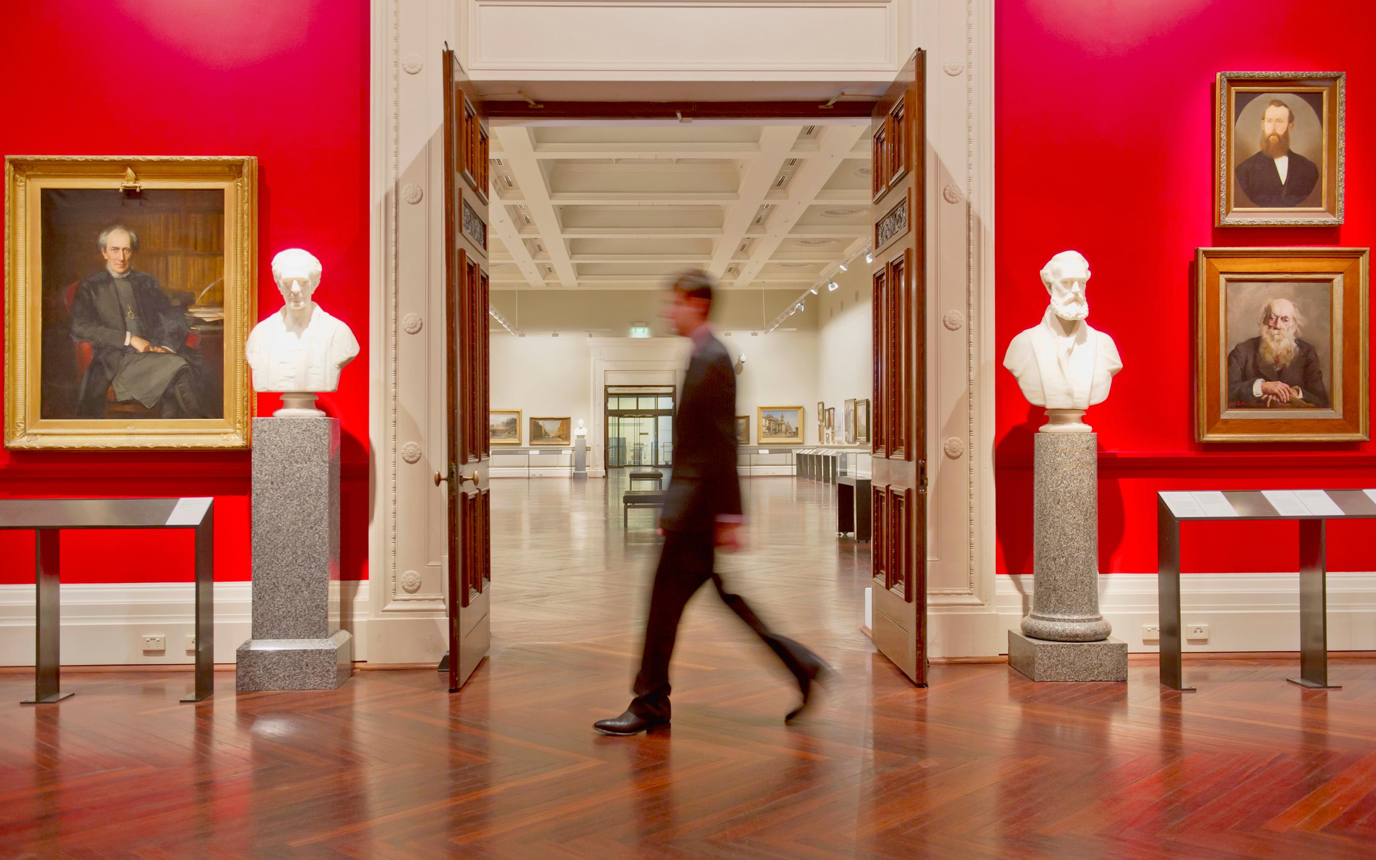 A person walking through a bright, professional art gallery featuring various framed portraits and sculptures.
