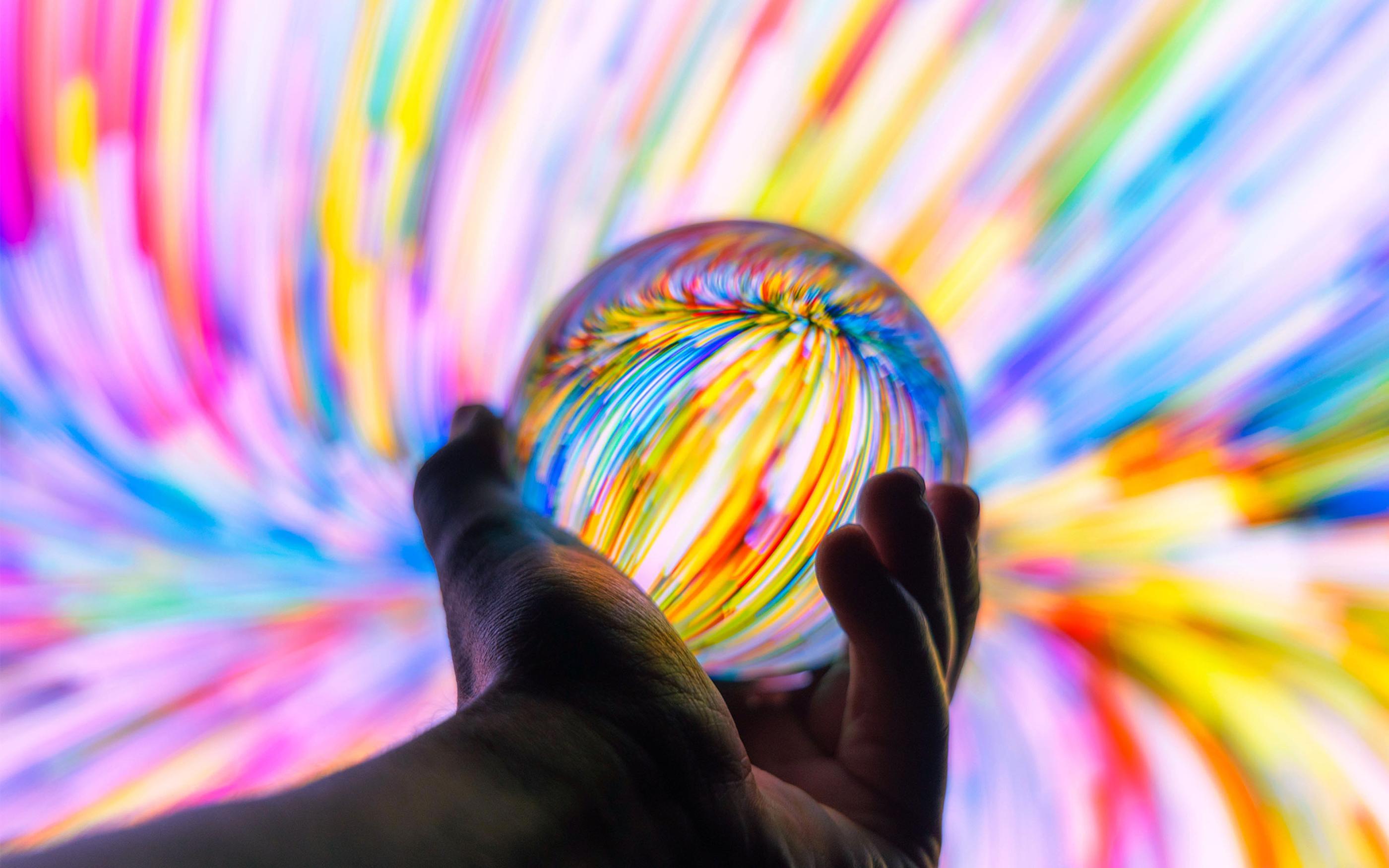 Holding a crystal ball through colorful background at night.
